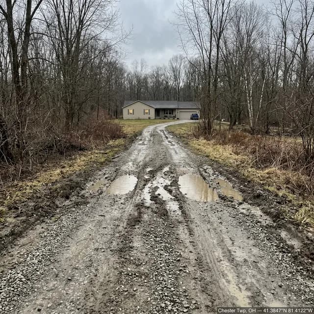Rutted gravel driveway in Chester Township, Ohio before restoration — deep muddy wheel tracks holding standing water, with loose stone pushed out to the shoulders