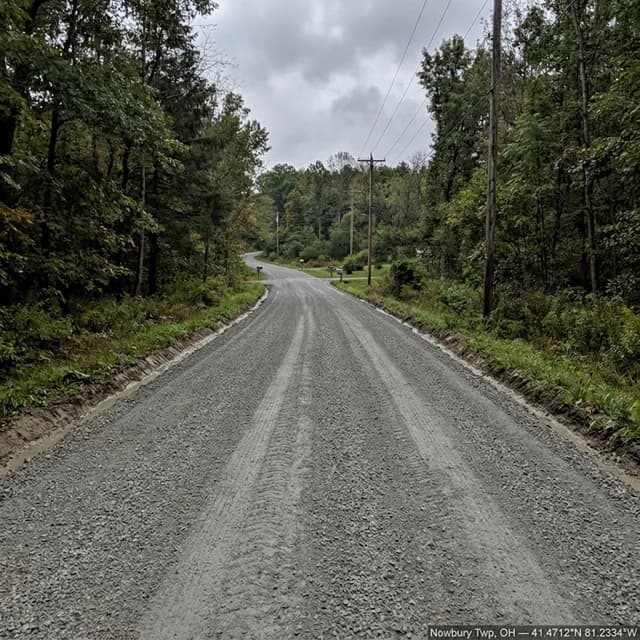 The same Newbury Township, Ohio private lane after restoration — one continuous crowned gravel surface with clean shoulders, photographed in the rain