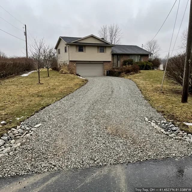 The same sloped Troy Township, Ohio driveway after restoration — full even gravel cover from the garage to the road, with heavier stone edging holding the shoulders