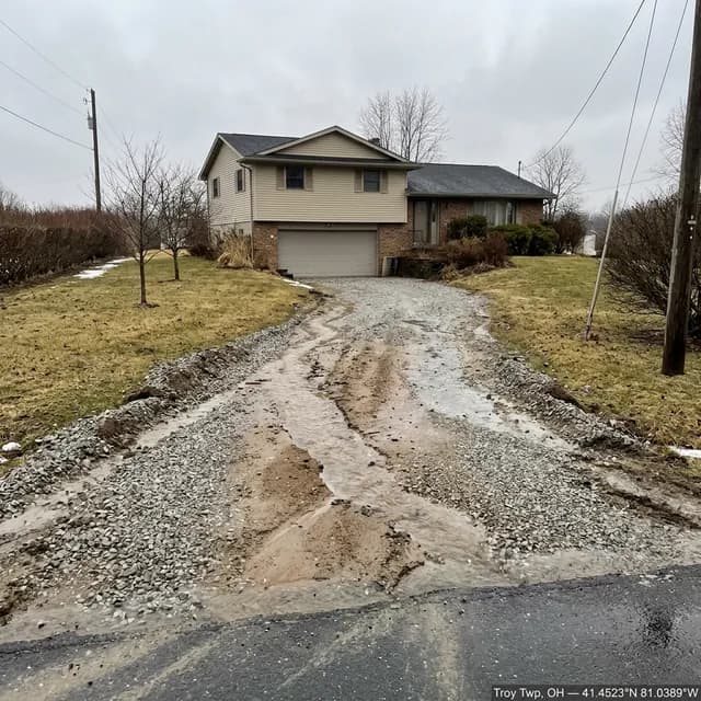 Washed-out gravel driveway in Troy Township, Ohio before restoration — runoff channels cut down the slope with surface stone carried out toward the road