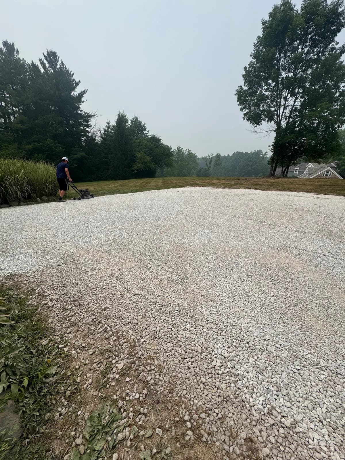 Finished gravel parking pad covered in even new stone, with a crew member mowing along the lawn edge