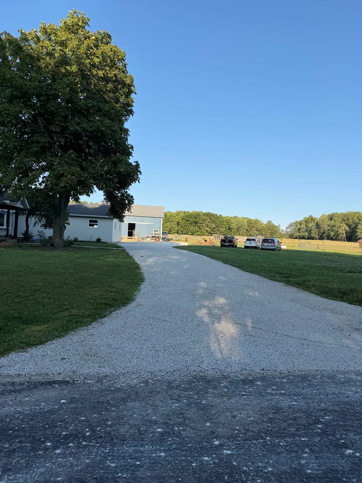 The same driveway after GravelBoss work, seen from the road: clean edges and a smooth, even stone surface leading to the house and barn