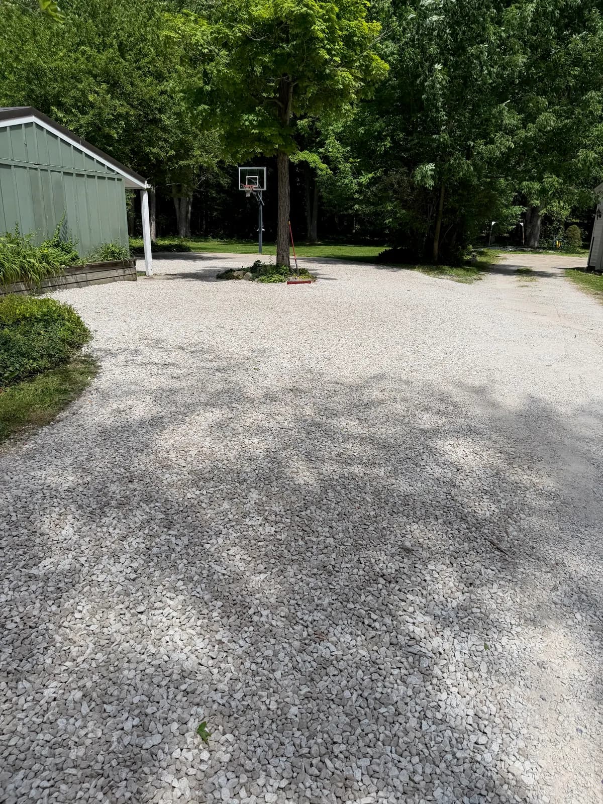 Finished gravel driveway with an even stone surface beside a green garage, under trees
